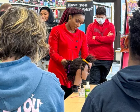 Students gather around Lana as she braids a mannequin's hair in the Library.