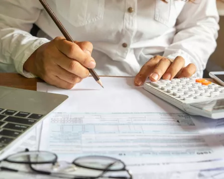 Woman in front of a laptop with a calculator filling out tax forms