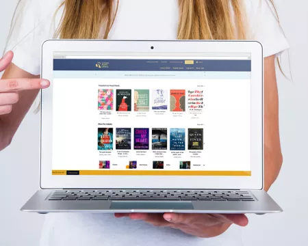  A woman holds a laptop, pointing at the screen which displays London Public Library's catalogue.