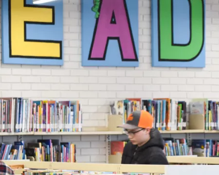 Teens browse the stacks at Byron Library under a sign that says READ.
