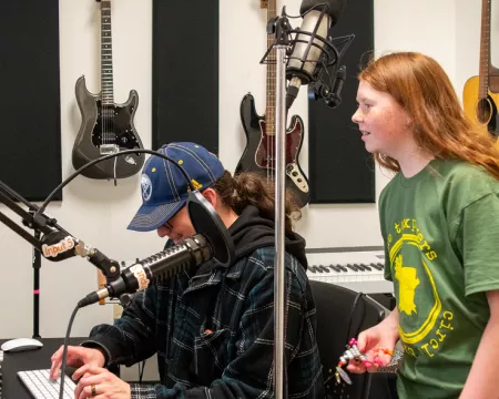 Isaak stands next to his dad in front of a computer in the Central Library recording studio.