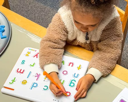 A young girl sits at a table with books, letters, and literacy activities.