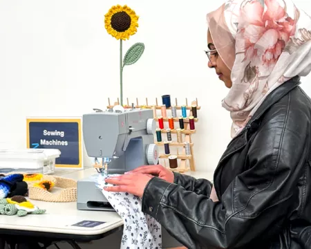 Nourhan sitting and sewing at the Library sewing machine in the Labs