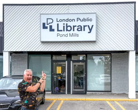 Kevin Moore stands in front of Pond Mills Branch Library, pointing at the front doors.