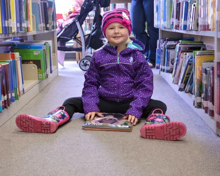 A young girl sits with a book on the carpet in Pond Mills Branch Library.