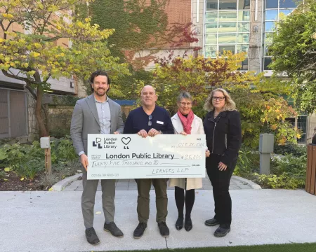 A representative from Lerners LLP stands with three representatives from London Public Library in the Rotary Reading Garden holding a large cheque for twenty five thousand dollars.