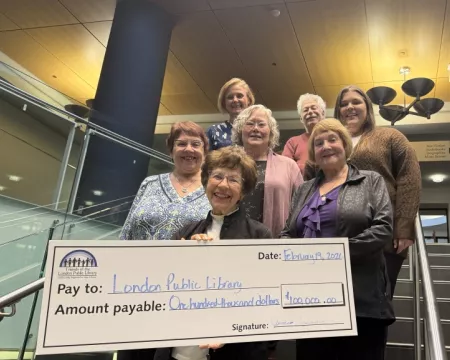 Three members of the Friends executive are joined by four members of the Library board on the stairs at Central Library. Carmen Sprovieri, Friends President stands in front holding a cheque for $100,000 made out to London Public Library.