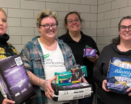 4 people standing in a public washroom holding period products
