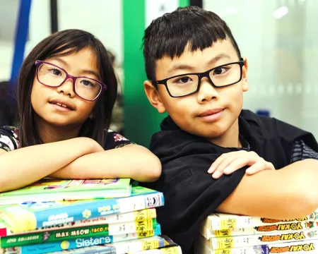 Two children cross their arms on a stack of books