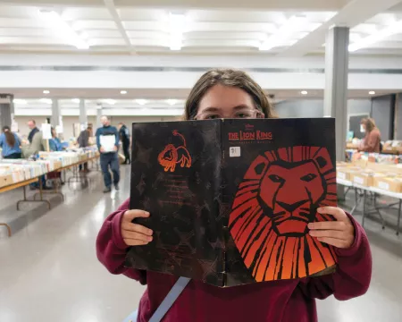Person holding a copy of The Lion King at a large book sale.