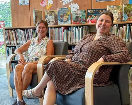 Two smiling women sit on chairs in the children's area of Crouch Branch Library with bookshelves in the background.