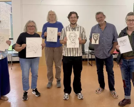six people stand each holding a self portrait drawing on white paper
