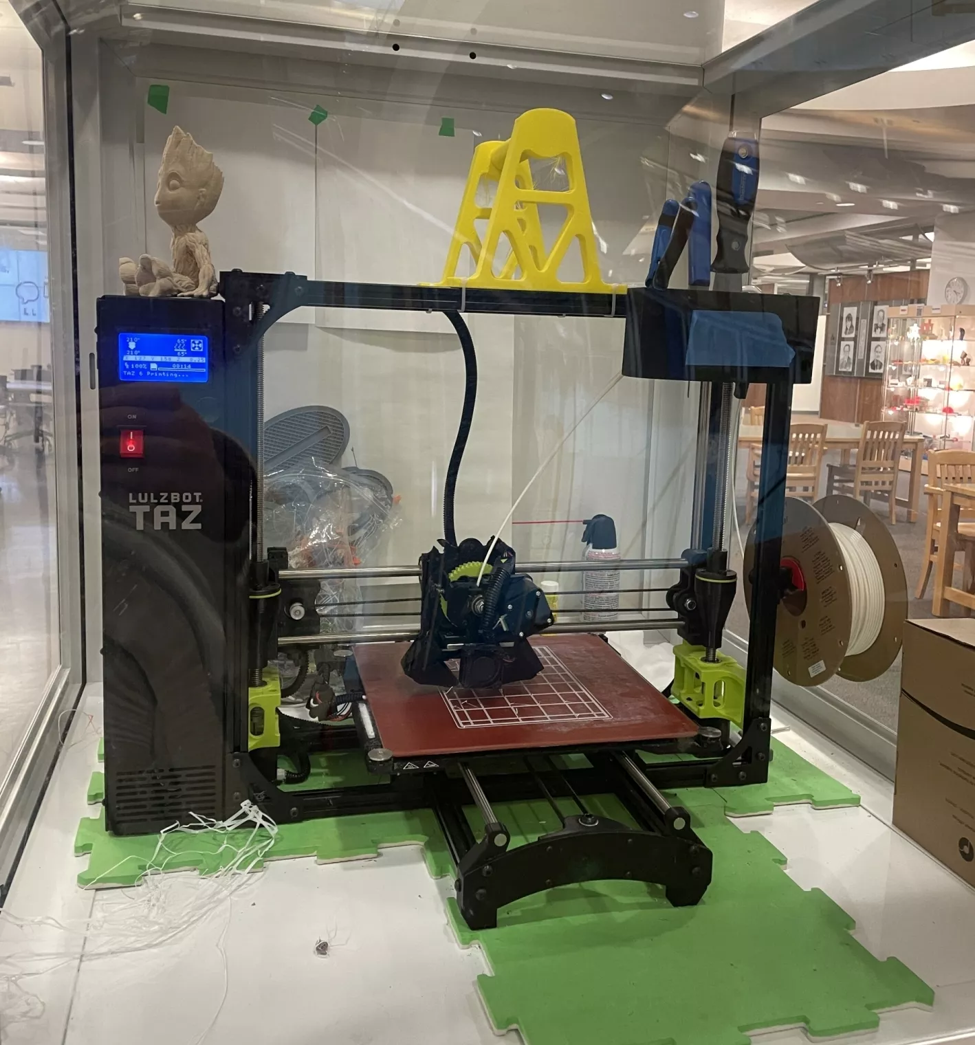 Photo of a Lutzbot Taz 3D printer in a case at the Library. On top of the printer are 3D printed objects.