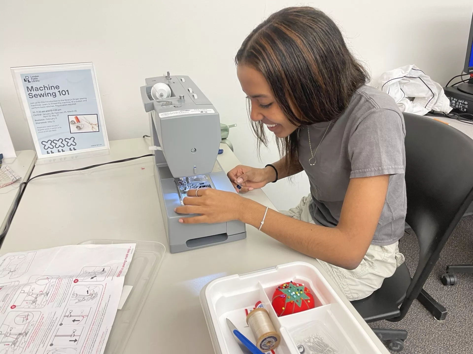 Photo of a young woman using a sewing machine and smiling as she threads the needle.