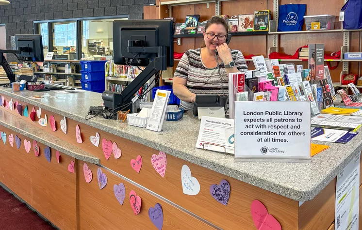 A staff member answers the phone behind the front desk at Crouch Branch Library, where paper hearts made by local kids decorate the desk.
