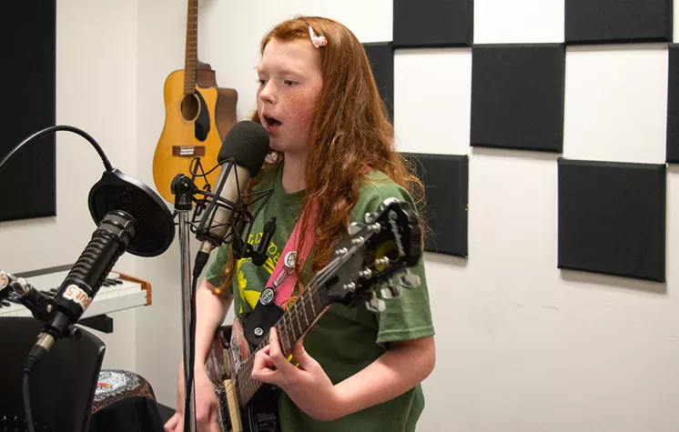 Isaak playing his electric guitar at a microphone recording music in the Central Library recording studio.
