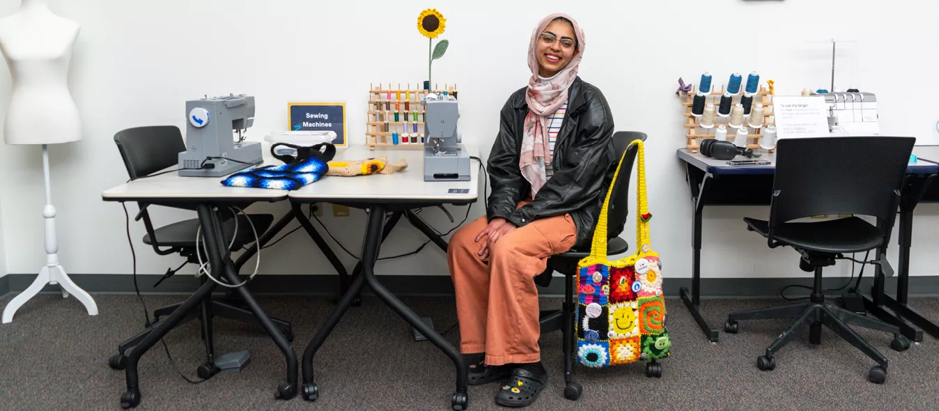 Nourhan sitting at the sewing machine table in the Central Library labs
