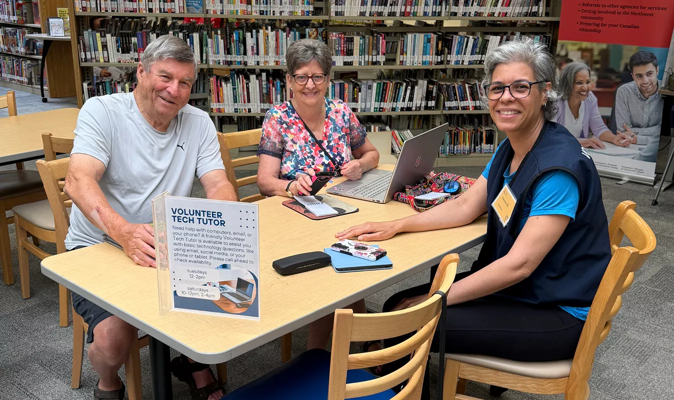 Volunteer tech tutor across from two older adults with their laptop and phone