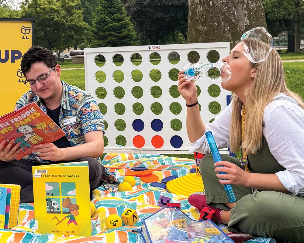 two librarians at an outdoor pop up reading books and blowing bubbles