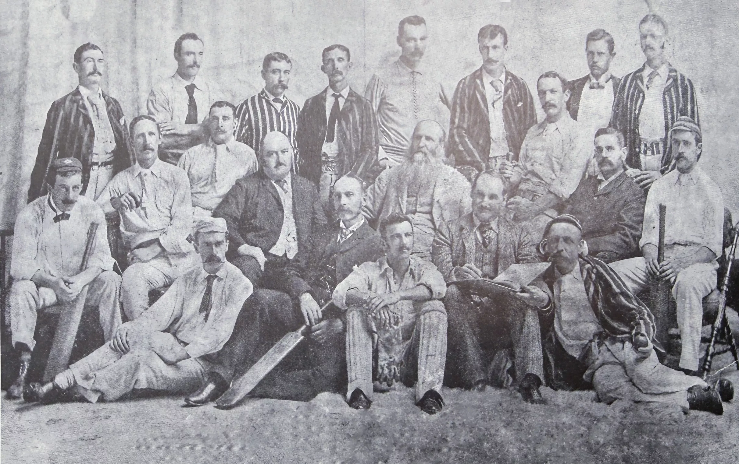 Balck and white undated photo of Cricket players in white uniforms and caps, some wearing striped balzers and some in full suites.