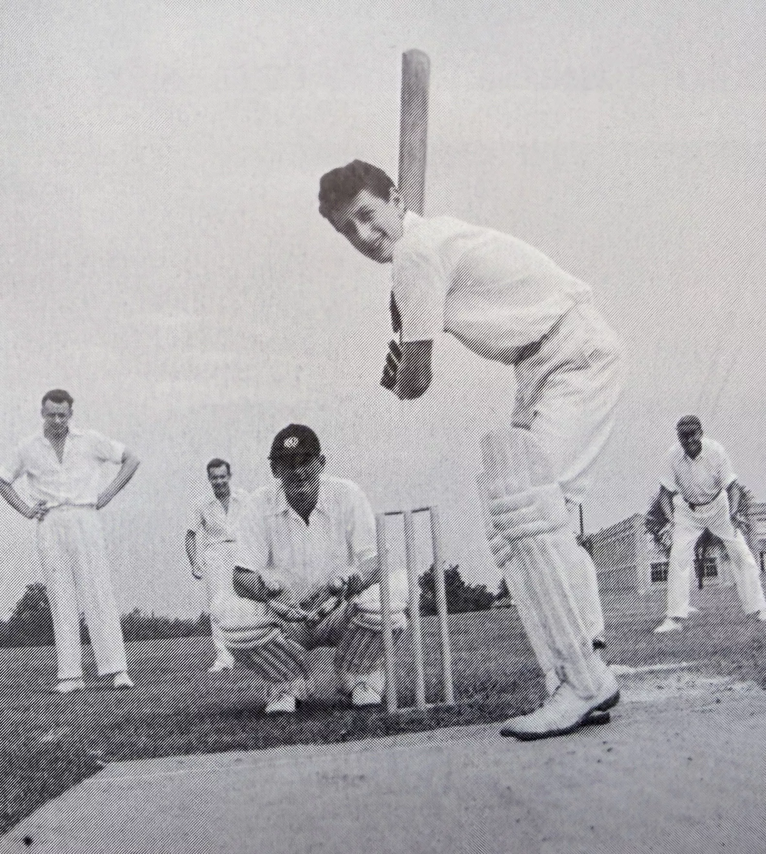 Black and white photo of a cricket player at bat with players in behind.
