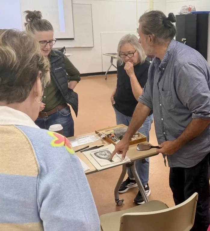 Four people stand looking at a drawing on a table.